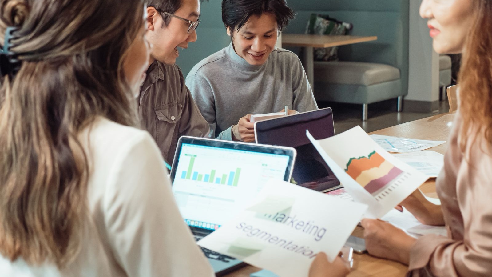 Group of colleagues discussing marketing strategies with charts and laptops in an office setting.