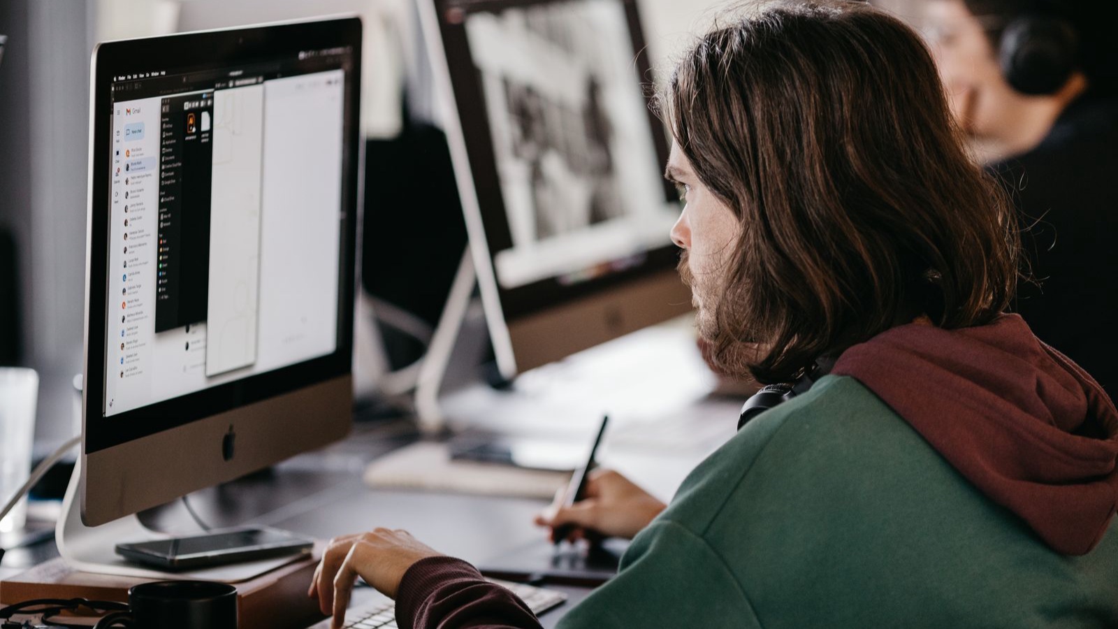 Writing Service Pages: Explain the Work and Its Scope Clearly Person in a hoodie working at a desktop computer in an office setting, focused and engaged.