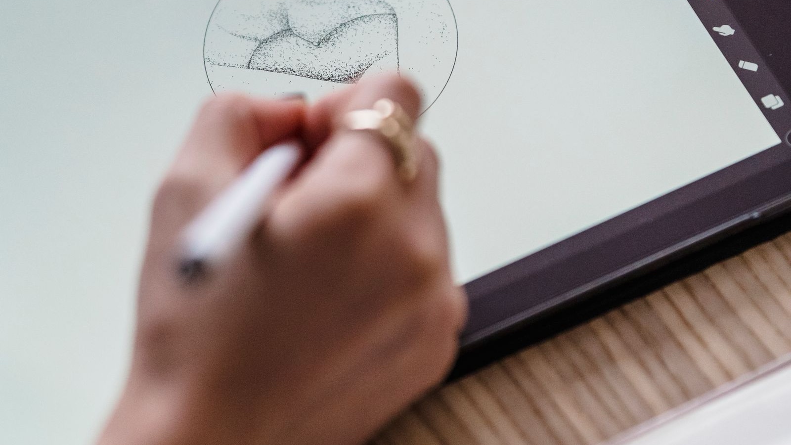 A close-up of an artist's hand sketching on a digital tablet in a creative workspace.