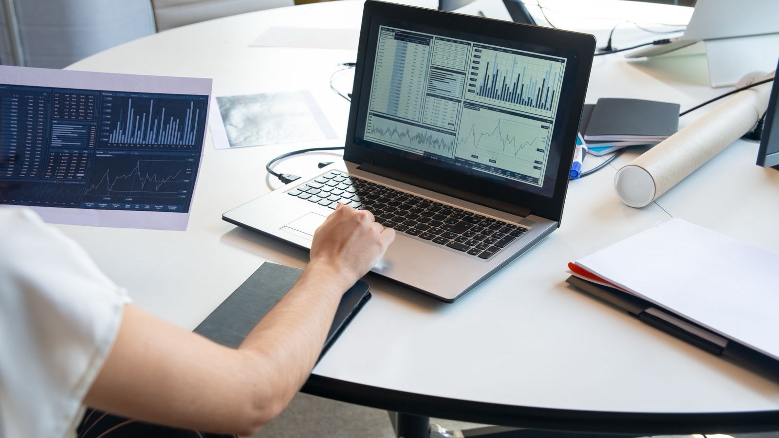 A person reviewing financial graphs on a laptop and printed documents